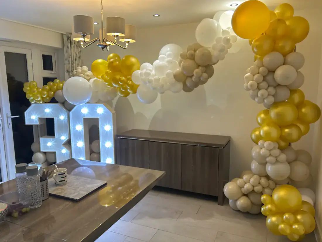 Gold and white balloon arch with 30 light up numbers in a kitchen