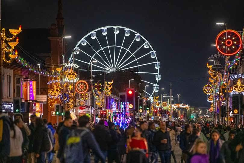 Crowds celebrating Diwali beneath Leicester's festival lights and illuminated observation wheel