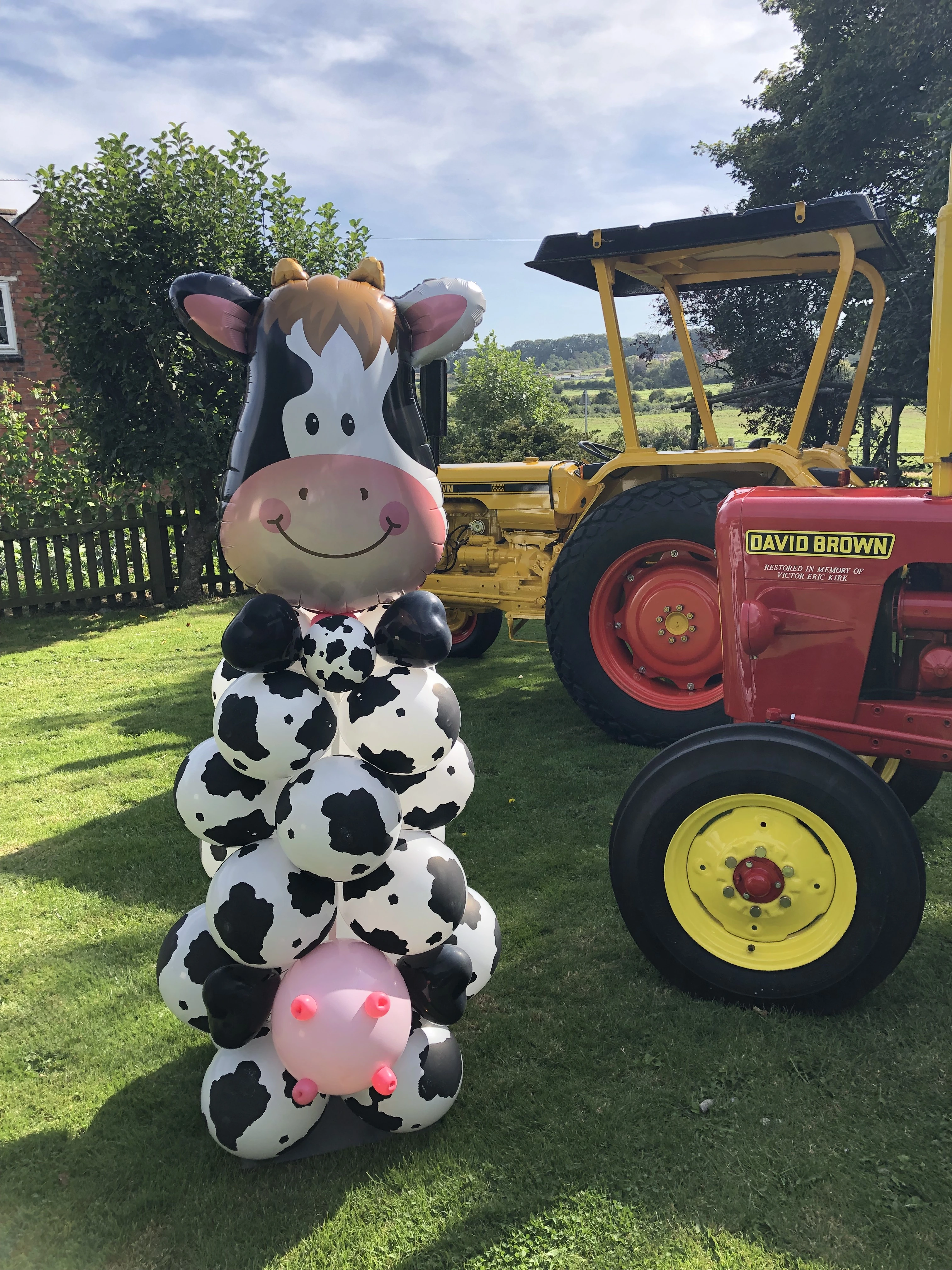 Cow themed balloon character beside a tractor at a branded outdoor event